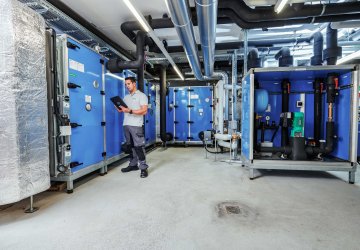 Technician monitoring HVAC machinery via tablet in an industrial maintenance setting.