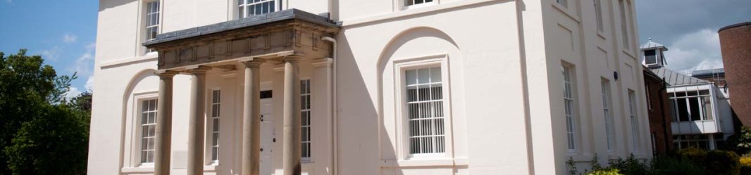 A beige neoclassical building with a flat roof, columns, and arched windows under a blue sky.