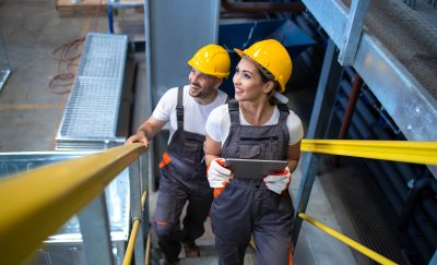 Two maintenance workers climbing stairs in a factory.