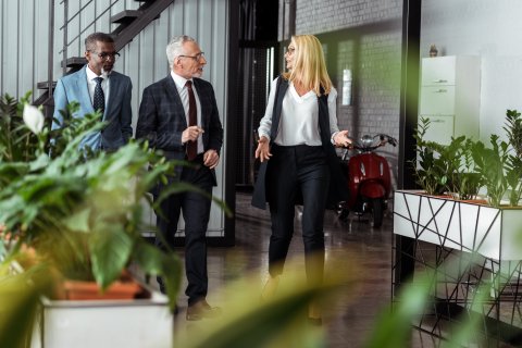 Three business professionals having a conversation while walking in a plant-filled office.