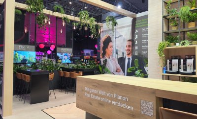 Empty Planon Real Estate exhibition stand with seating areas, digital displays and plant decorations.