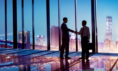 Two businessmen shaking hands in glass office building.