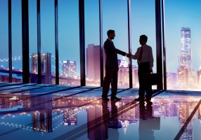 Two businessmen shaking hands in glass office building.