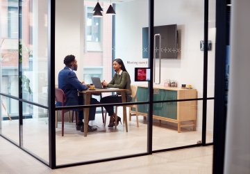 Two people in a meeting room inside a workspace with glass walls..