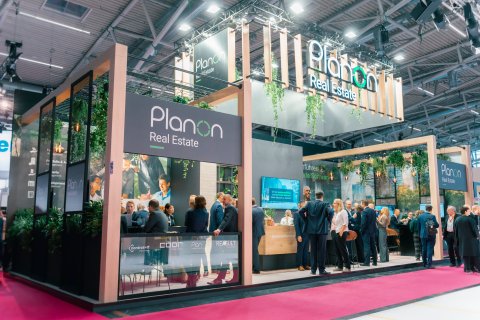 Two people in a conversation at an exhibition booth with screens in the background.