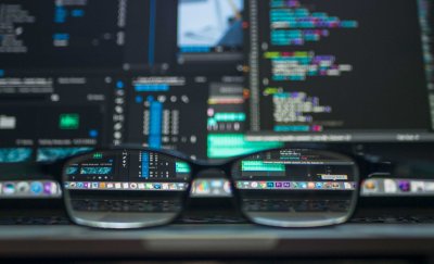 Glasses on desk in front of computers with coding on the screens