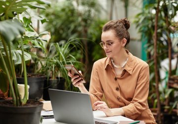 Young smiling businesswoman in brown blouse scrolling in mobile phone.