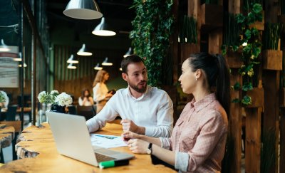 People discussing a plan while sitting on a table with an open laptop.