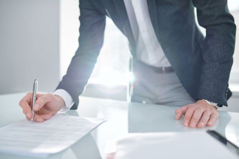 Close-up of a businessman signing paperwork with sunlight reflecting on the desk.