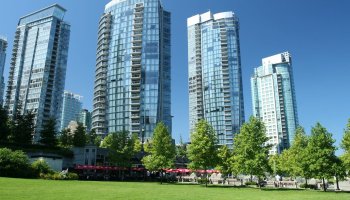 Multiple tall buildings with many windows behind a green area.