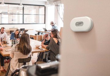 People discussing at a table, indoor air quality sensor at the wall.