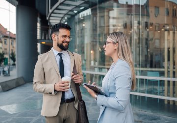 Two business professionals engaged in a casual conversation, standing in a modern office environment.
