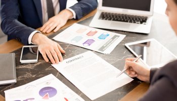 Data graphics on a desk with a man signing a contract