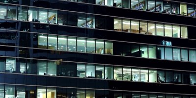 Nighttime view of an office building with illuminated workspaces visible through large windows.
