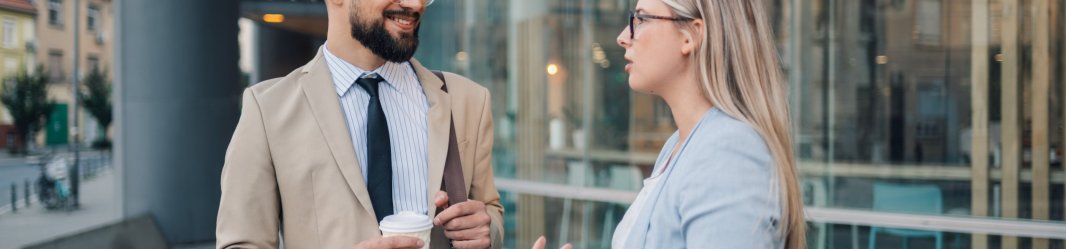 Two business professionals engaged in a casual conversation, standing in a modern office environment.