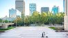 Tall real estate buildings in the back with persons walking through a park.