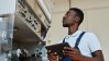 Factory worker inspecting machinery while holding a tablet for digital maintenance checks.