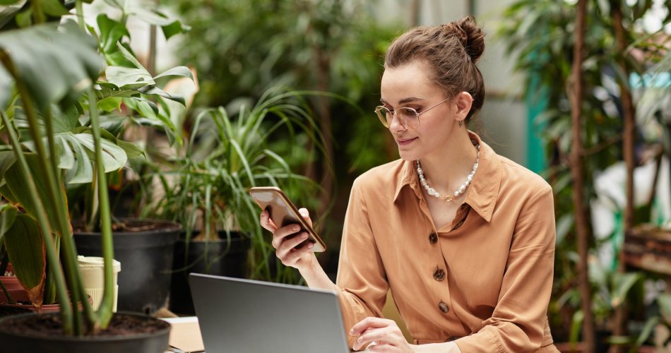 Young smiling businesswoman in brown blouse scrolling in mobile phone.