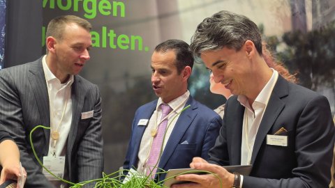 Group of attendees in conversation at the Planon Real Estate stand.
