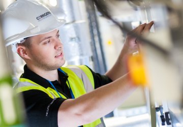 Maintenance professional in a safety vest and hard hat working on equipment in an industrial setting.